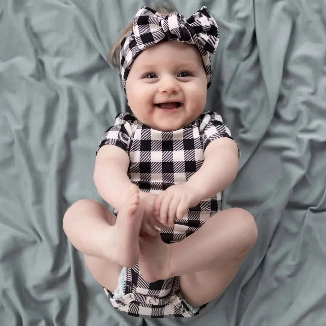 Smiling baby in checkered outfit wearing a short sleeve bamboo onesie for newborn apparel