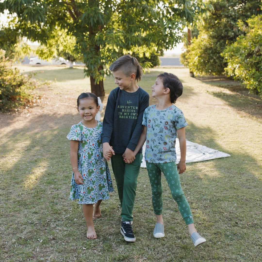 Three children in a grassy area wearing kids bamboo t-shirts