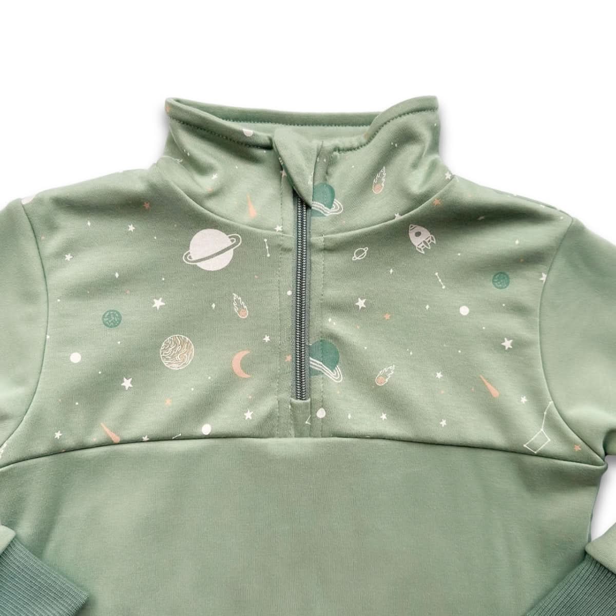 The Kids Bamboo Fleece Half-Zip by Little & Lively is a light green, Canadian-made pullover with a cozy half zip and high collar. It features pastel planets, rockets, stars, and moons on top with a solid green bottom for playful style.