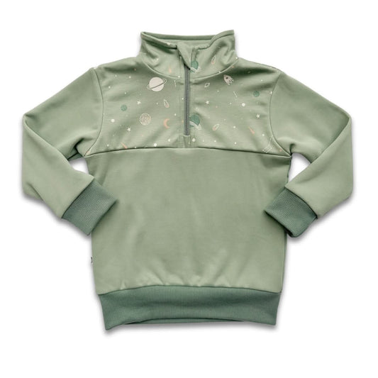 A young girl with long dark hair sits cross-legged on the floor wearing a purple and navy floral-patterned Kids Bamboo Fleece Half-Zip by Little & Lively, ethically made in Canada. A green plant is partially visible in the background.