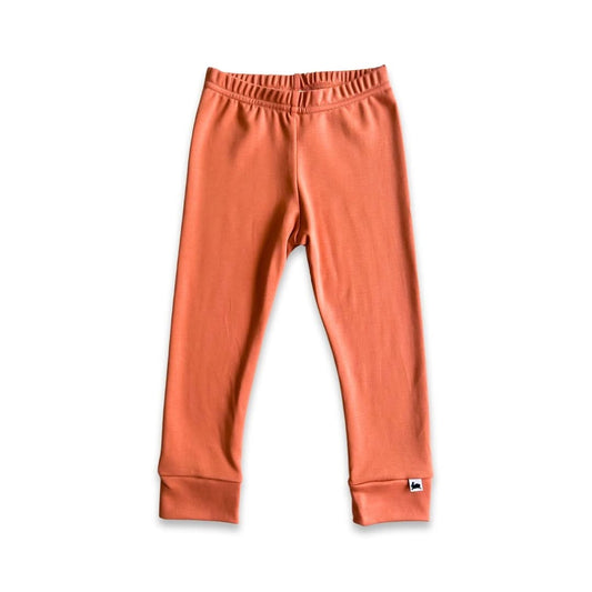 A pair of orange Baby Bamboo Leggings by Little & Lively, made in Canada with an elastic waistband and cuffed ankles. Shown on a white background with a small white tag featuring a dark logo on one ankle.