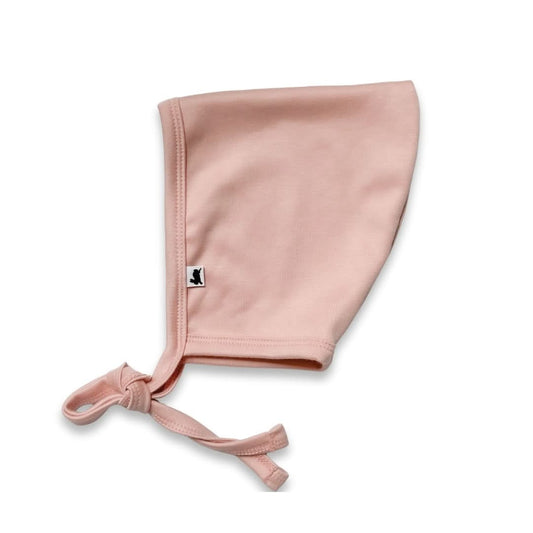 The Little & Lively Bamboo Baby Pixie Bonnet is light pink, brimless, crafted from soft bamboo fabric, and features a tie strap plus a small black and white bird logo tag on the side, shown against a white background.