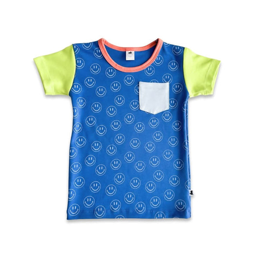 The Little & Lively Baby/Kids Bamboo Pocket T-shirt in Blue Smilies features yellow color-blocked short sleeves, a blue body with white smiley faces, coral neck trim, and a white chest pocket, shown on a white background.