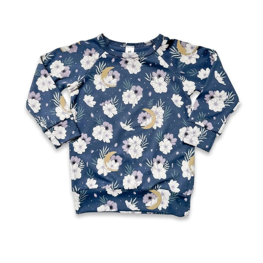 The Little & Lively Baby/Kids Bamboo Raglan Pullover | Prints is a cozy long-sleeve top with a navy base and white, beige, and lavender floral design, shown laid flat on a white surface.