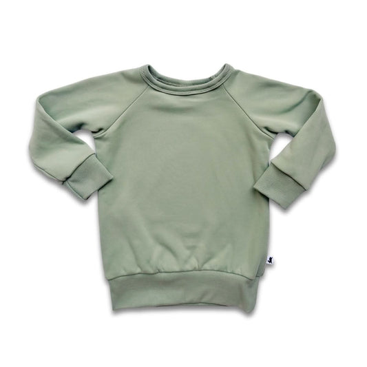 The Little & Lively Baby/Kids Bamboo Fleece Raglan Pullover is a light sage green, long-sleeved crewneck with ribbed cuffs and hem. Ethically made from soft bamboo fleece, it features a small white side tag. Shown laid flat on a white background.