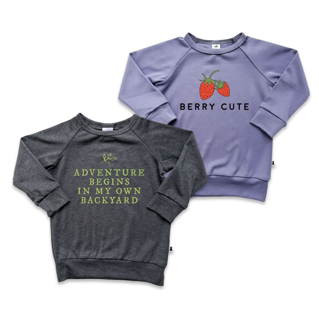 Two Little & Lively Youth Graphic Bamboo Raglan Sleeve Pullovers are shown: one gray with "ADVENTURE BEGINS IN MY OWN BACKYARD" in green, and another lavender with two strawberries and "BERRY CUTE" in black.